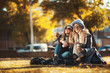 Two beautiful happy women sitting in the park on grass drinking coffee and laughing. Concept friendship, togetherness, happiness. Having fun on coffee break with best friend.