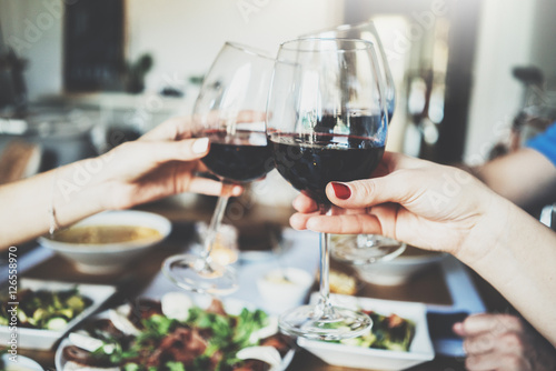 Fotografie, Obraz Young happy friends cheering with glasses of red wine, family dinning at home, e