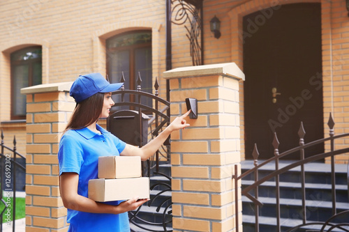 Photographie Female courier in uniform ringing in doorbell