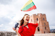 Portrait of a young female tourist with lithuanian flag in front of the famous old tower in Vilnius. Woman having great vacations in Lithuania