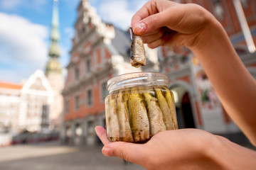 Wall Mural - Female hands holding a jar with sprats in the center of Riga city. Riga is famous for it's tasty golden and smoked fish called sprats.