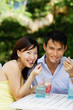 © Alexander - Couple sitting side by side, eating, smiling at camera