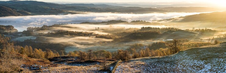 Wall Mural - vibrant golden sunlight shining over hills covered in autumnal mist in the lake district.