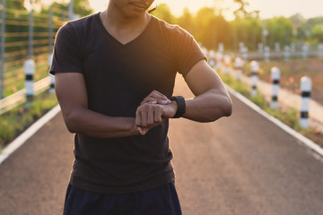 running man looking sport watch. male runner jogging using smart-watch in evening.