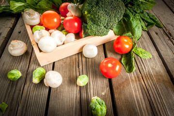 Fresh raw organic vegetables on a rustic wooden table in basket: spinach, broccoli, Brussels sprouts, tomatoes, mushrooms, champignons. 