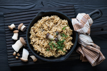 Wall Mural - Frying pan with porcini risotto over black wooden background