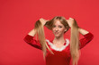 © Rudkov - Beautiful young woman in Santa costume playing with a strand of her long silky hair, looking at camera on red background