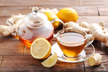 Cup of tea with ginger root and lemon on brown wooden table