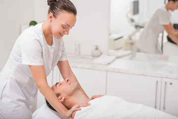 Joyful masseuse massaging male shoulders