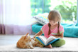 © Africa Studio - Red cat and cute little girl reading book on carpet