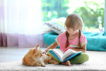 Red cat and cute little girl reading book on carpet