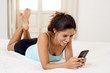 © Wordley Calvo Stock - hispanic woman relaxed using internet mobile phone sending message at home bedroom smiling happy