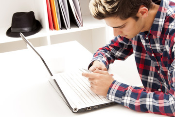 young man with cellphone and laptop at home