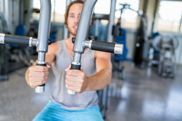 Wall Mural - Gym machine closeup on male hands. Male athlete training chest muscles on fitness equipment pec deck fly working out strength alone indoors. Man holding handles of fitness machine at gym center.