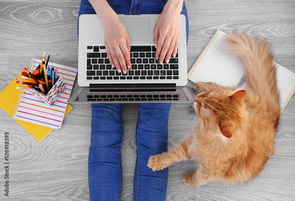 Woman typing on laptop and sitting on floor with fluffy cat