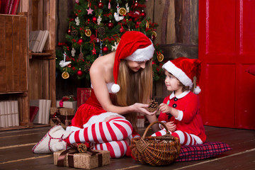 Wall Mural - Two Santa girls decorating Christmas tree having fun. New year interior. Xmas atmosphere, family celebrating holidays.