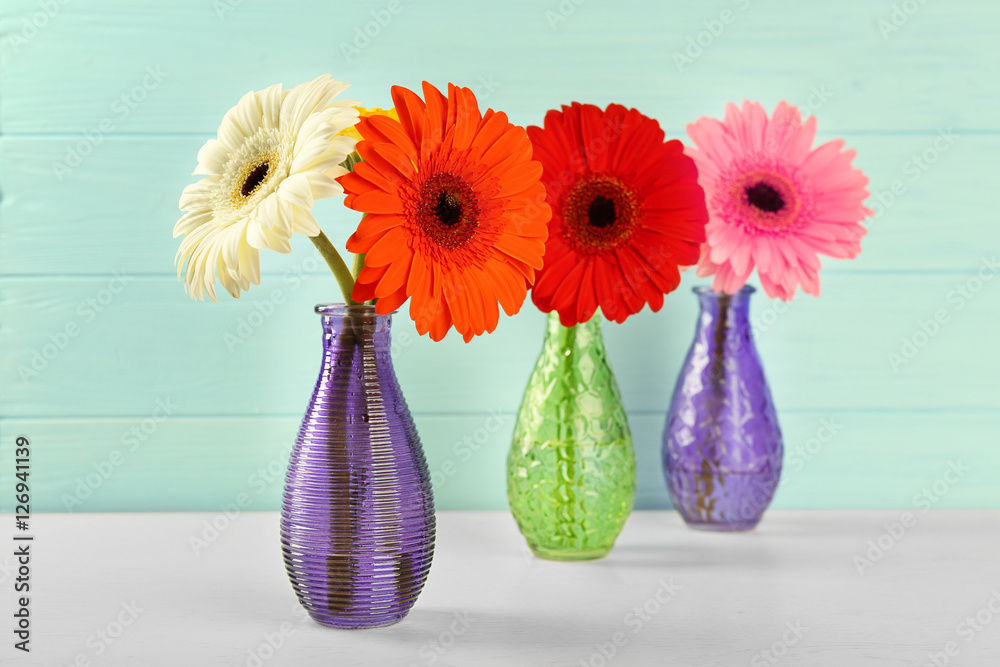 Beautiful gerbera flowers in vases on blurred wooden background