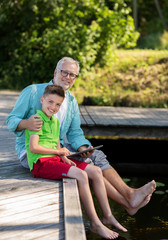 Poster - grandfather and boy with tablet pc on river berth