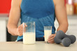 Young sporty man with jug, glass of fresh milk and dumbbells at kitchen, closeup