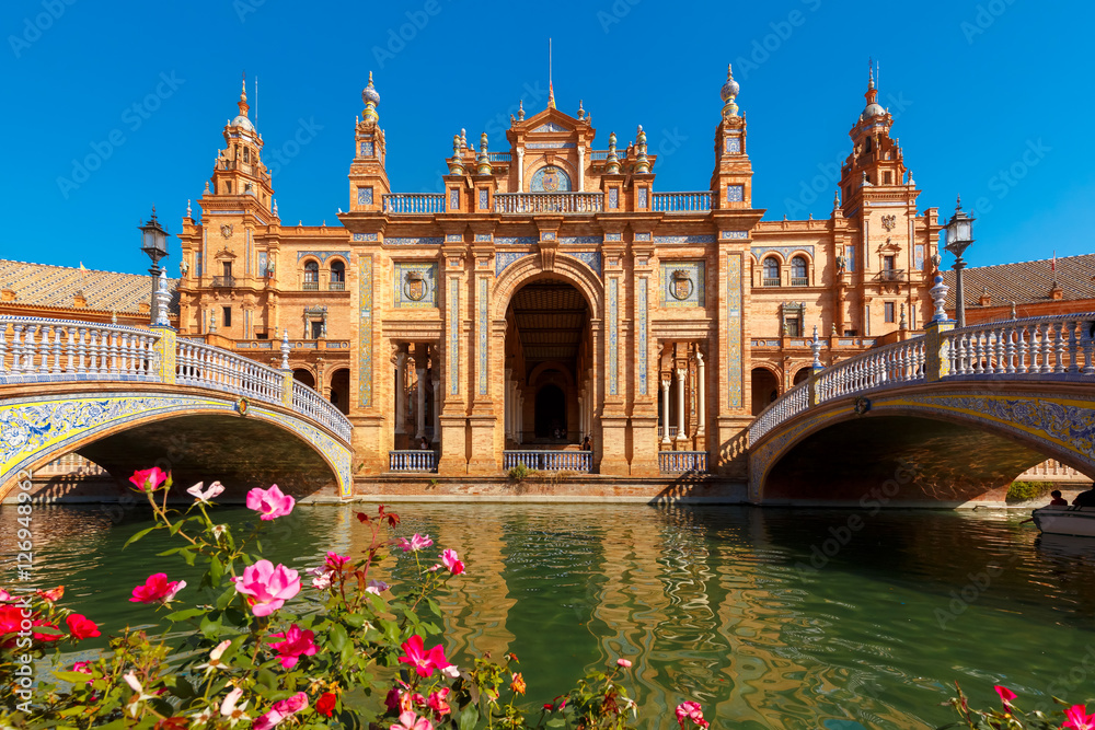 Spain Square or Plaza de Espana in Seville in the sunny summer day, Andalusia, Spain. Flower beds, bridges and channel in the foreground - obrazy, fototapety, plakaty 