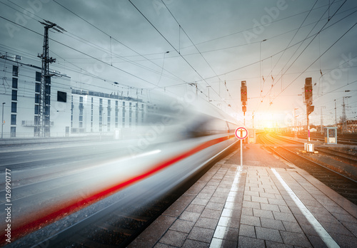 Fotomural Tren de pasajeros de alta velocidad en la vía de ferrocarril en movimiento al atardecer