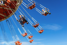 Mother With The Six-year-old Son Ride An Attraction On A Swing Agains The Blue Sky In Amusement Park