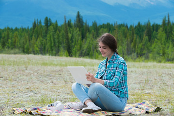 Beautiful girl in a field on mountains, using  tablet pc.