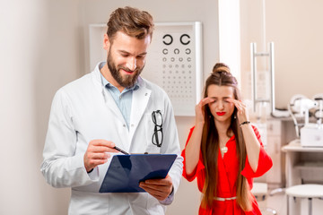 Eye doctor writing medical recipe standing in the cabinet with unhappy female patient. Eye diseases and problems with vision