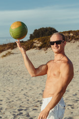 slender man in shorts with a volley ball on the beach, white sand