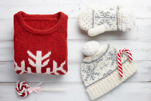 Winter Holiday Knitted Sweater, Mittens, Cap And Christmas Lollipops On White Wooden Background