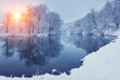 Leinwandbild Motiv Winter forest on the river at sunset. Panoramic landscape with snowy trees, sun, beautiful frozen river with reflection in water. Seasonal. Winter trees, lake and blue sky. Frosty snowy river. Weather