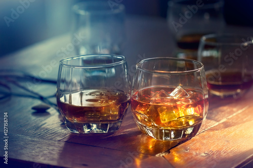 Cuadros en Lienzo Whiskey bourbon in a glass with ice on wooden table colorful background