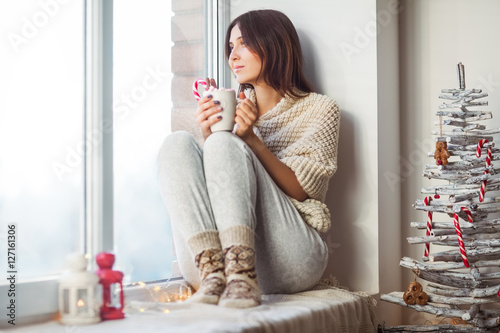 Fotografía Happy beautiful woman drinking hot coffee sitting on window sill
