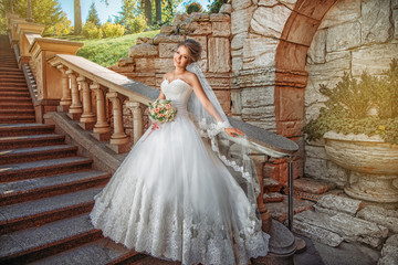 Beautiful, happy bride in white wedding dress is standing near stone staircase