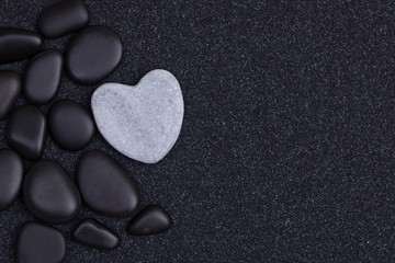 Black stones with grey zen heart shaped rock on  grain sand