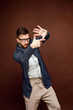 Young casual man putting hands in gesture of camera and pretending to make picture on brown background.
