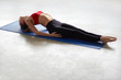 © kegfire - Side view of a young woman lying on the yoga mat at gym