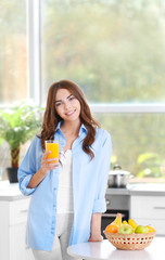 Poster - Beautiful young woman with glass of orange juice standing at kitchen