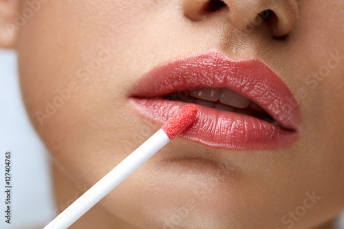 Leinwand Poster Beauty Makeup. Beautiful Woman Applies Lip Gloss