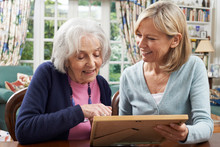 Senior Woman Looks At Photo In Frame With Mature Female Neighbor