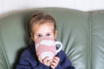 Girl Child in Warm Sweater Sitting Under a Blanket and Drinking 