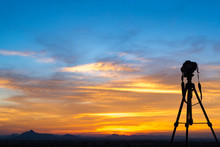 A Camera Set On A Tripod Aimed At A Silhouette Of A Landscape At Sunset