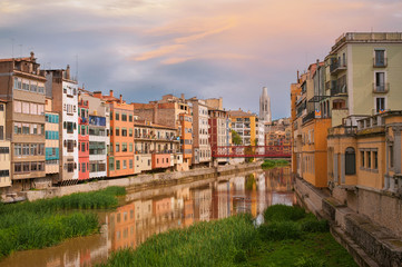 Colorful yellow and orange houses and bridge Pont de Sant Agusti reflected in water river Onyar, in Girona, Catalonia, Spain. Church of Sant Feliu and Saint Mary Cathedral at background.