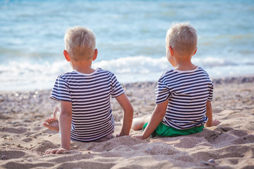 Two children in stripped vests sit by the sea