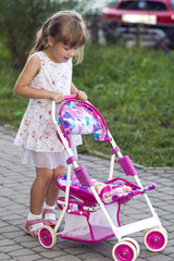 cute little girl with her toy carriage and doll outdoors