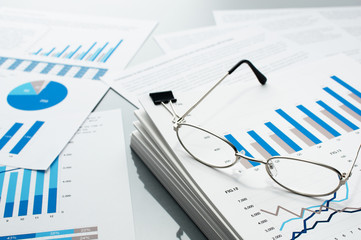 Poster - Checking business reports. Glasses and pile of documents. Many graphs and charts. Pile of documents on gray reflection background.
