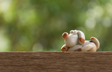 This ceramic doll sitting thinking about something. On wood background bokeh green from the leaves.