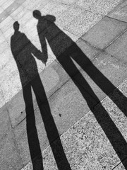 Black and white photo of shadow of a man and a woman holding hands.