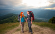 © anatoliy_gleb - Happy man and red-haired woman standing, looking to each other, holding hands, smiling on the road in the mountains on the background of the landscaped mighty mountains, forests, hills and clouds sky