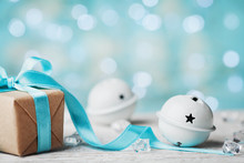Christmas Gift Box And White Jingle Bell Against Turquoise Bokeh Background. Holiday Greeting Card.